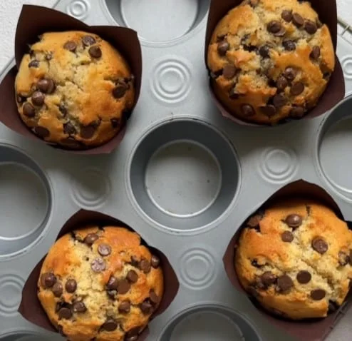 A muffin tray with freshly baked mini chocolate chip muffins in brown liners, just out of the oven