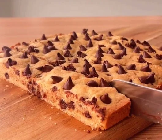 Freshly baked cookie sheet with chocolate chips, knife mid-cut on wooden board