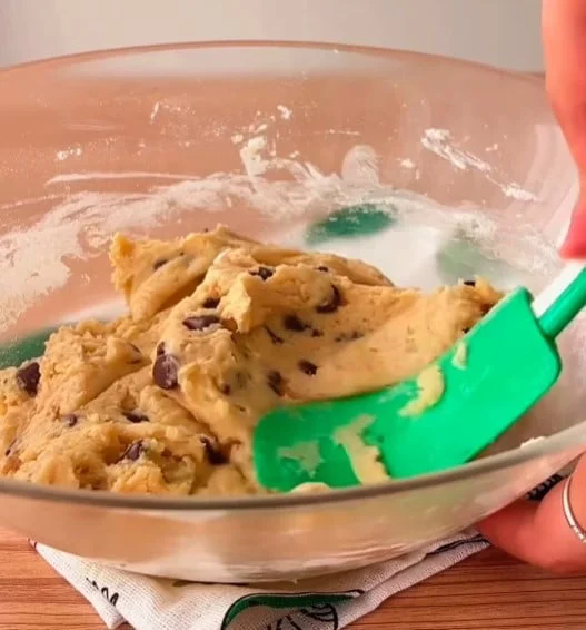 Bowl of cookie dough being mixed with a green spatula, flour dusted bowl