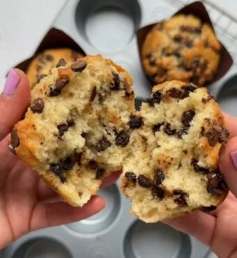 A freshly baked mini chocolate chip muffin split in half, revealing a fluffy inside dotted with chocolate chips
