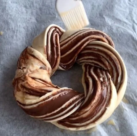 A nutella pastry wreath being brushed egg on top before going in the oven