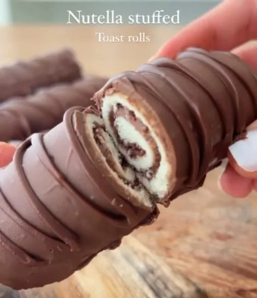 Hand holding a Nutella stuffed toast roll with layers visible, covered in a thick chocolate shell